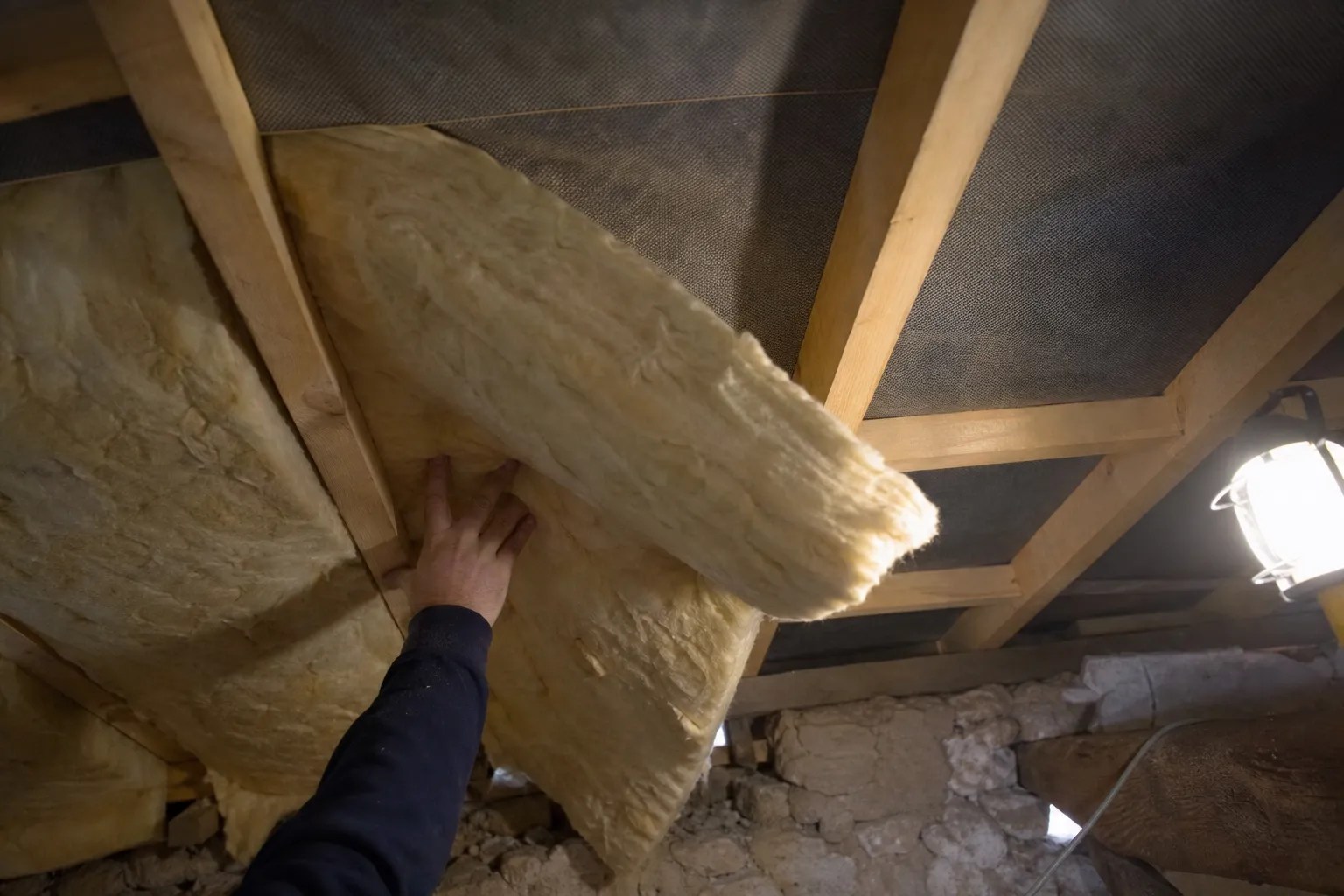 Comble en cours d’isolation, laine soufflée répandue sur le plancher entre les entretoises de bois